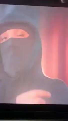 A low-resolution video shows a person in a hoodie, standing against a white background. The image is stylized with a light teal filter and horizontal lines that distort the figure. Yellow text in a foreign language appears on the screen, likely lyrics to a song. Later, the screen turns black and yellow text appears again, with the words "Yaxshi Yaman Uzm Oroliman." The video appears to be taken on a phone or tablet.