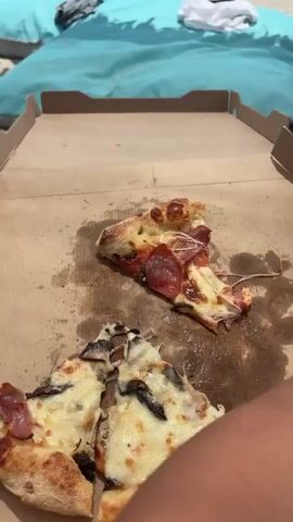 The video shows a group of people on a beach with pizza. The pizza is in a cardboard box, and it looks like there are two pizzas in the box. One pizza has pepperoni on it, and the other pizza has mushrooms and chicken on it. People are sitting on beach chairs, and there are drinks on a table. The video is taken from a low angle, and it is blurry in some parts. The video is about 4 seconds long.