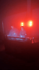 Two DJs perform under colored lighting in Milano venue