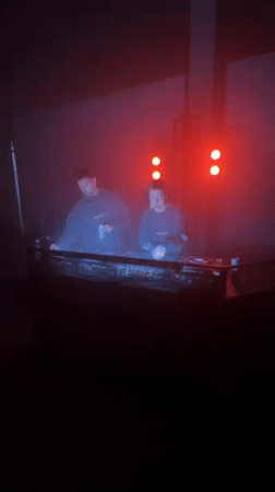 Two DJs perform under colored lighting in Milano venue