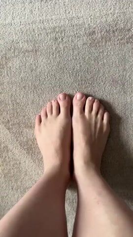 This video shows a pair of bare feet on a textured carpet. The feet are positioned with the toes pointing upwards and slightly spread apart. The camera is directly above the feet, providing a top-down view. The carpet appears to be a light neutral color with a subtle pattern. The lighting suggests an indoor setting, likely during the daytime. No other objects or people are visible in the frame. The feet are the sole focus of the video.