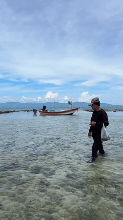 Wading through shallow water near an anchored boat in Thailand