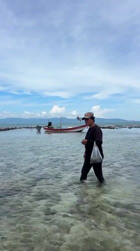 Wading through shallow water near an anchored boat in Thailand