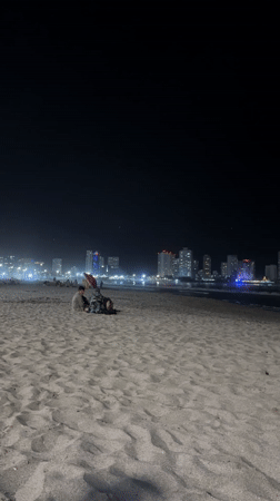Two people sit on beach at night near city