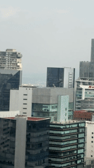 Dark helicopter flies over Mexico City buildings during hazy evening