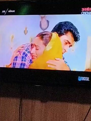 This is a video of a television screen displaying a scene from a film. The scene features a man and a woman embracing. The woman is wearing a yellow headscarf and a plaid shirt. The man is wearing a plaid shirt as well. The background appears to be an indoor setting. The screen also displays channel information and a logo.