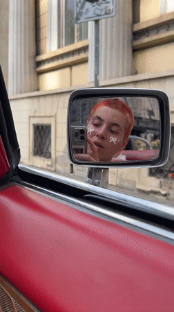 Person takes mirror selfie in red convertible at Belgrade traffic light