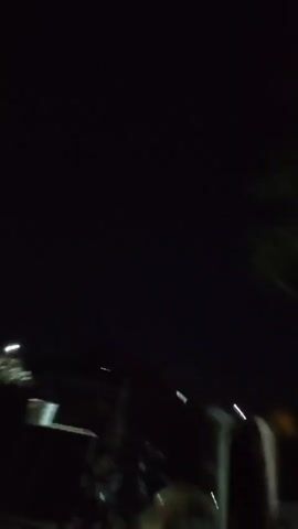 The video begins with a dark, out-of-focus shot of leaves against a black sky. The camera then pans down to reveal a dimly lit outdoor scene. In the foreground, there are several indistinct objects that appear to be large cylindrical containers, possibly bins or barrels, arranged in a row. The lighting is very low, making it difficult to discern details, but there are a few faint points of light in the background, suggesting artificial illumination. The overall impression is that of a nighttime scene in an outdoor storage or utility area. The video is very short and primarily features dark, grainy footage.