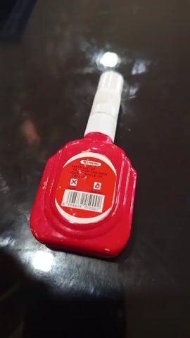 A small bottle of red correction fluid is on a black, shiny surface. The bottle is plastic and has a white applicator. The label on the bottle has warnings. It is not clear if anything happens after this.