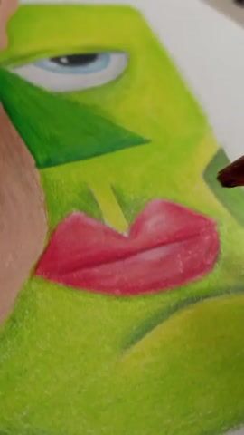 The video shows a close-up view of someone drawing on white paper with a colored pencil. The drawing features a person with green skin and red lips. The eye is light blue with a dark blue pupil. The drawing style appears to be somewhat abstract. The hand of the person drawing holds a colored pencil and adds shading to the red lips.