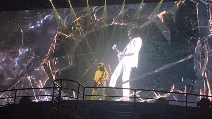 Yellow-clad guitarist performs on dark stage with shattered glass backdrop
