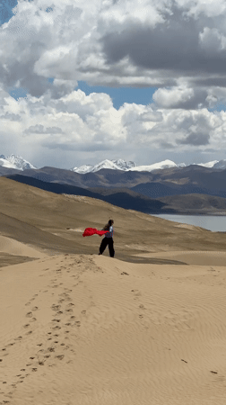 Person plays with red fabric across sand dunes in Labrang
