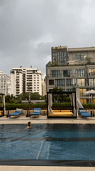 Person swims in Bangkok rooftop pool amid urban skyline
