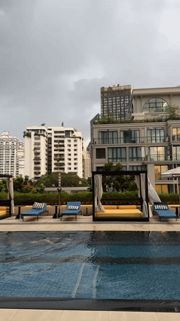 Person swims in Bangkok rooftop pool amid urban skyline