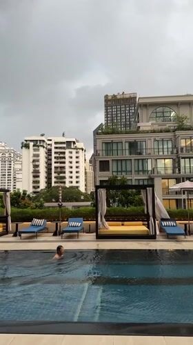 Person swims in Bangkok rooftop pool amid urban skyline