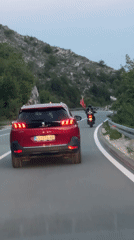 Motorcyclist waves red flag behind SUV on Montenegro mountain road