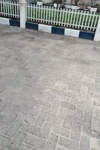 The video shows a paved area with a white fence. The paving stones are laid in a herringbone pattern. The fence is white with black and white striped posts. In the background, there are trees and buildings. The video appears to be taken from a high angle, looking down at the paving and fence. The lighting is overcast.