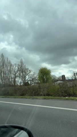 A car is driving on a road on a cloudy day. There are fields on either side of the road. A sign indicates "Beernem" is 400 meters away.