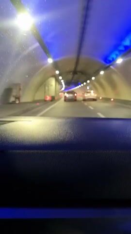 The video is filmed from inside a vehicle, showcasing a journey through a well-lit tunnel. The foreground is dominated by the textured, dark dashboard of the car. Through the windshield, the tunnel stretches ahead, illuminated by numerous bright white lights embedded in the ceiling and distinctive blue strip lighting along the upper edges of the tunnel walls. The walls themselves appear to be light-colored, possibly white or off-white.

Multiple lanes of traffic are visible, with several cars ahead, their taillights glowing red in the distance. A red directional arrow sign is briefly visible on the left side of the tunnel. The overall impression is of a modern and clean infrastructure. The time of day appears to be dark, suggesting night or very early morning, as artificial lighting fully illuminates the environment.

A person speaking Russian can be heard, stating, "Что в Москве, что в Стамбуле, всё одинаково," which translates to "What's in Moscow, what's in Istanbul, everything is the same," providing a verbal cue connecting to the given location context of Fatih, Turkey.