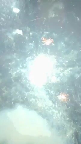 This video shows a nighttime fireworks display. The first few seconds capture bright red and gold fireworks exploding in a dark sky. The following seconds show smaller, sparser fireworks, with some yellow sparks against the black. The video ends with a few faint sparks in the distance. There is some smoke visible at the bottom of the screen throughout the clip.