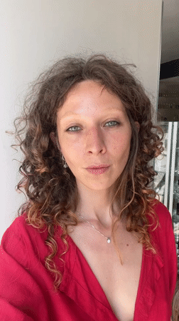 Close-up portrait in Tel Aviv, red top, playful expression.