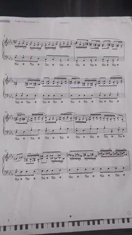 A person plays a piano. The sheet music is visible on the piano. The music is written in treble and bass clefs. The notes on the staff are visible and appear to be complex, with many sharps and accidentals. The player's hands are not visible, but the keys of the piano are being pressed. The video is filmed from a high angle, looking down at the piano and sheet music. The lighting is dim, and the image quality is poor. The video is short, only a few seconds long.