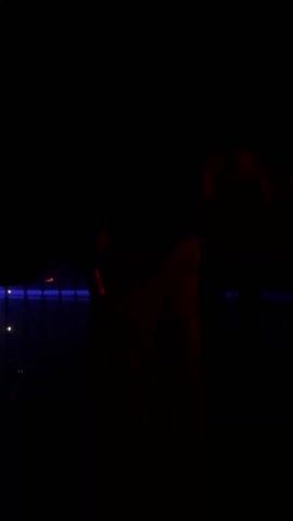 The video takes place in a very dark environment. The predominant color is black. Sporadically, faint blue and red lights illuminate elements within the frame, including some horizontal structures and possibly a caged area.  No people are clearly visible, only vague shapes are suggested. No specific actions or interactions can be discerned. The focus seems to be on capturing the sparse lighting in an otherwise obscured scene.