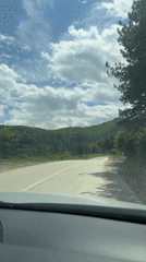 Vehicle travels rural road through Bulgarian woodland under clear skies