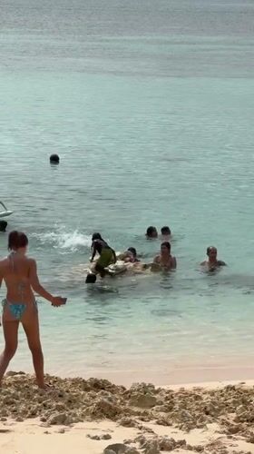 Woman photographs swimmers in turquoise waters at General Luna beach