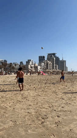 Beachgoers play volleyball on sunny Tel Aviv beach