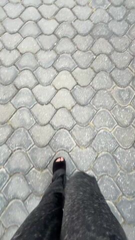 A person wearing black slippers and a long gray garment is walking on a gray brick walkway. The bricks are shaped in a wave pattern. The video is shot from a first-person perspective, looking down at the person's feet as they walk.