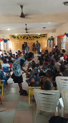 Children's gathering documented at school hall with colorful seating