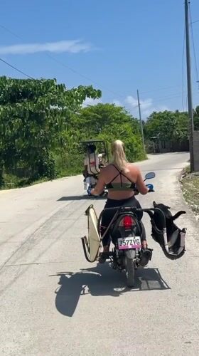 Woman rides surfboard-equipped scooter in General Luna, Philippines