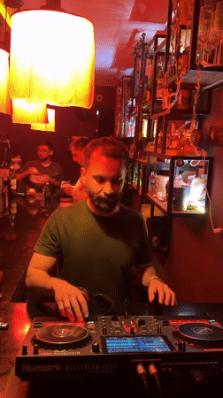 DJ operates mixing equipment behind bar with staff present