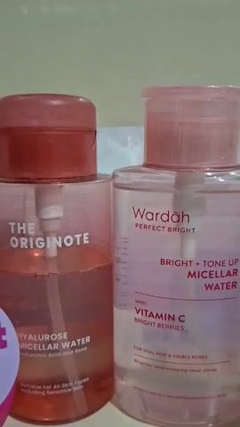 The video presents a static, medium shot of a collection of skincare products arranged on a white shelf. The products include micellar water from brands like "THE ORIGINOTE" and "Wardah", a "bright glow" moisturizer by "Emina", "Facetology" triple care sunscreen, "Tazzi" 3in1 whitening body lotion, and "SKINTIFIC" niacinamide brightening essence. Behind the products, there is a sheet mask pack labeled "JESTHAM". The products are arranged against a light gray wall. The shot remains still throughout the video.