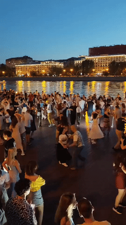 Partner dancing on a Moscow riverfront at dusk