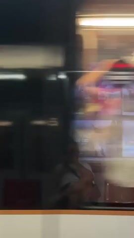 This video captures a blurred, dynamic view from inside a public transportation vehicle, likely a train or tram, moving through Molenbeek-Saint-Jean, Belgium. The scene is dominated by motion blur, obscuring fine details but suggesting a bustling environment.

The primary subjects are indistinct figures of people, seen through windows as passengers or individuals outside the vehicle. Their forms are rendered as streaks of color due to the rapid movement. We can discern hints of their clothing, with some appearing to wear lighter colored tops. The interior of the vehicle is illuminated by bright, horizontal fluorescent lights, creating highlights and reflections on the surfaces. Red seats are visible in the foreground, providing a grounding element amidst the blur.

The activity taking place is transit. The camera appears to be looking out from within the moving vehicle, or possibly at reflections on its exterior, as the scenery outside rushes by. There are also glimpses of what could be advertisements or signage on the interior walls of the transport.

Notable details include the consistent bright lighting, suggesting it is either daytime or the interior is well-lit, contrasting with the potentially darker exterior. The motion blur creates a sense of speed and the passage of time. While specific emotions are hard to discern due to the blur, the overall impression is one of movement and urban transit. No legible text is visible due to the image quality and motion. The location context places this scene within the urban landscape of Molenbeek-Saint-Jean, Belgium.