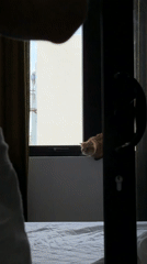 Orange cat watches from window while woman makes bed