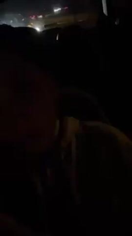 A person is in a car at night. The interior is dark. The person is looking at the camera. Music is playing.
