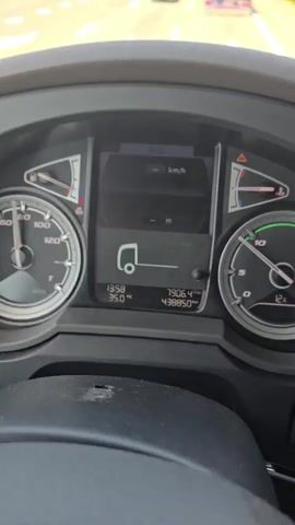 The video shows the interior of a truck cab, with a view of the road ahead through the windshield. The dashboard instruments are visible, including a speedometer and a tachometer. The truck is driving on a highway, and there are other vehicles on the road, including cars and another truck with a shipping container. Overhead signs indicate directions to various cities and routes, including Amsterdam, Rotterdam, Utrecht, and Vlaardingen. The weather appears to be clear and sunny. The video is a first-person perspective from the driver's seat.