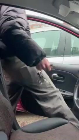 A man in a car, wearing a black winter coat and a dark gray beanie, enters the driver's seat. He turns to look at the camera. He says "Coucou," then "Bonjour." The camera angle is from inside the car. It appears to be cold outside, possibly snowing.