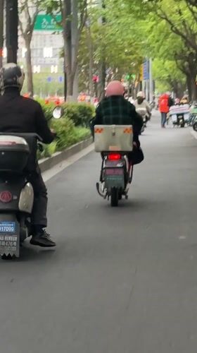 Scooter riders navigate tree-lined Shanghai street during overcast morning