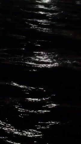 The video shows a dark body of water, likely at night, with ripples and reflections of light on the surface. The light source appears to be overhead, casting bright streaks across the water. The overall impression is one of movement and light play on a dark, liquid surface.