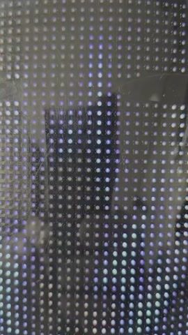 This video is a close-up shot of a grid of small, circular lights, likely LEDs, against a dark background. The lights are predominantly in shades of blue and white, with some appearing to glow more intensely than others. There is a faint reflection on the surface, obscuring some of the lights. The arrangement of the lights is uniform, forming a pixelated pattern. The overall impression is abstract, focusing on the texture and light output of the illuminated grid.