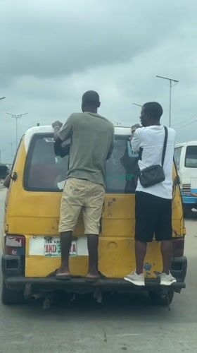 Two people riding on the back of a yellow van in Agbara