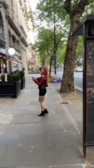 Woman in red jacket smiles at observer on London sidewalk