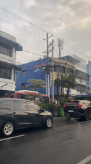 Mixed traffic moves through a cloudy city street near local shops.
