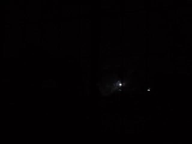 The video shows a very dark scene, possibly outdoors at night. The primary light source seems to be a bright, concentrated light, possibly a streetlight or the moon, positioned in the middle ground. The foreground and background are largely obscured by darkness, making it difficult to discern specific details about the environment or any other objects or people present.