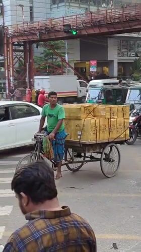 Cyclist hauls cardboard boxes through busy Dhaka intersection