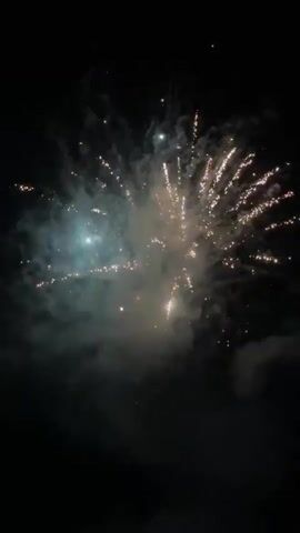 The video displays a dark night sky illuminated by multiple fireworks. Several fireworks launch from the bottom of the frame, ascending into the dark sky before exploding into large, bright, golden-yellow bursts with starburst patterns and trails of light. Smoke from the explosions is visible against the dark background. The scene consists solely of the night sky and the bursting fireworks.